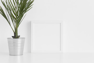 White square frame mockup with a palm in a pot on a white table.