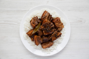 Homemade Filipino Adobo Pork with rice on a white plate over white wooden surface, top view. Flat lay, overhead, from above. Close-up.