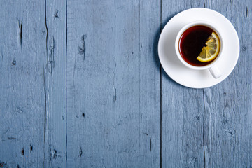 White cup of tea with lemon on a blue gray wooden background, top view, empty space