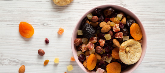 Top view, dried fruits and nut mix in a pink bowl on white wooden surface. Overhead, from above, overhead.
