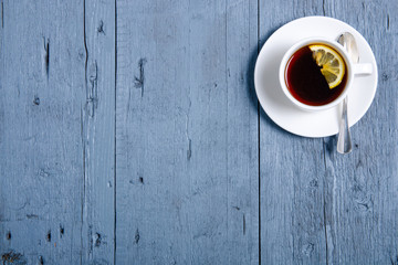 White cup of tea with lemon on a blue gray wooden background, top view, empty space