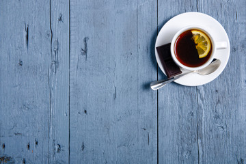 White cup of mint tea with lemon and chocolate on a blue gray wooden background, top view, empty space