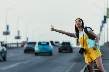 beautiful and asian woman in yellow overalls hitchhiking and holding map