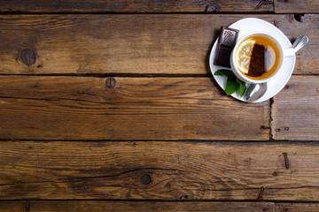 White cup of mint tea with lemon and chocolate on a brown wooden background, top view, empty space