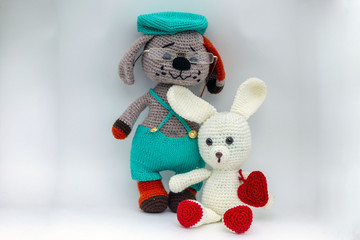 Amigurumi dog in a cap and glasses together with a hare with a heart posing for the photographer.