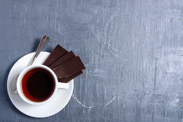 White cup of tea with chocolate on gray stone table background, top view, empty space