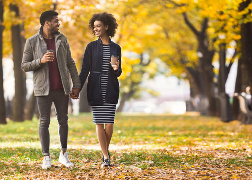 Happy african-american couple with coffee cups walking in park