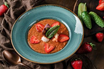Delicious gazpacho soup with shrimps, strawberries and cucumber in bowl over brown wooden background. Healthy food, clean eating, dieting, top view