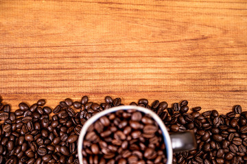 Coffee beans over a wooden table top with a coffee mug full of beans.