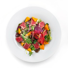 Healthy salad with seared tuna fish, greens, bell pepper and sauce in plate on isolated white background. Healthy food, clean eating, dieting, top view