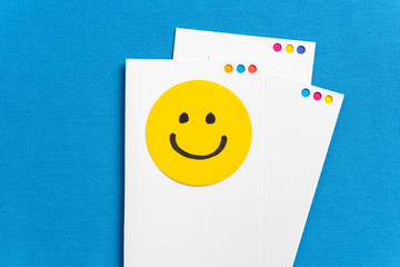Notes with yellow circle happy smiling face cartoon on paper screen card and blue texture background. Happy work day concept.