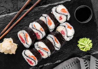 Sushi rolls and maki set with salmon and tuna fish, cheese and wasabi on black slate background. Japanese cuisine, close up