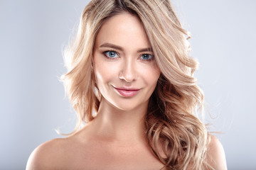 Fototapeta premium Blonde young woman with healthy curly hair and natural make up . Beautiful model girl with wavy hairstyle. Care and beauty