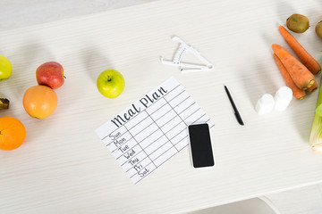 top view of meal plan, smartphone with blank screen, pills, caliper, pen and fresh food on wooden surface