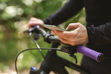 Cropped imafe of cyclist holding bike and using smartphone