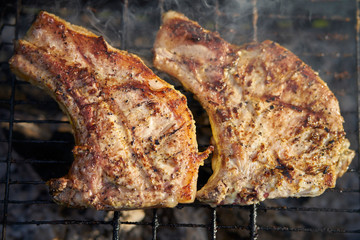 two pork steaks on a grill with smoke grilled on coals