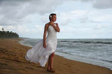 Girl in a white dress meets the sunset on the beach of the tropical ocean. Young girl looks into the distance