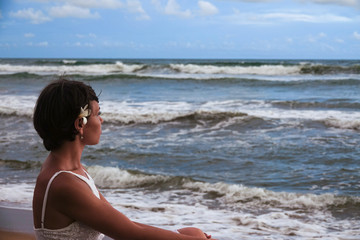 Fototapeta na wymiar Portrait of a girl who looks into the distance against the background of the tropical ocean. A young girl sits on the beach and looks into the distance
