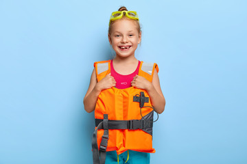 Small beautiful girl ready for boat trip, wears goggles and lifevest, has fun on vacancy, plays at...