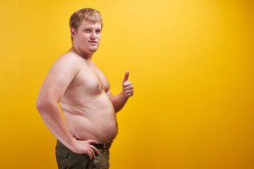 Huge young man with big fat belly and naked body in profile. Concept of obesity, fast and junk...