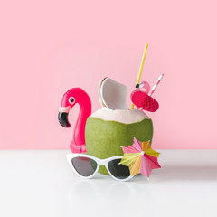 Fresh coconut on a pastel pink background with flamingo inflatable drink holder and sunglasses, summer vibes concept
