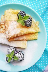 Delicious hot pancakes with blackberries and mint on a wooden background.