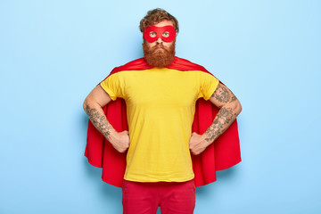 Photo of serious male in superhero costume, keeps hands on waist, possesses extraordinary talents,...