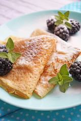 Delicious hot pancakes with blackberries and mint on a wooden background.