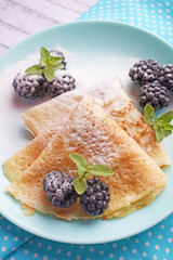 Delicious hot pancakes with blackberries and mint on a wooden background.