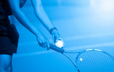 A tennis player prepares to serve a tennis ball during a match. Blue filter