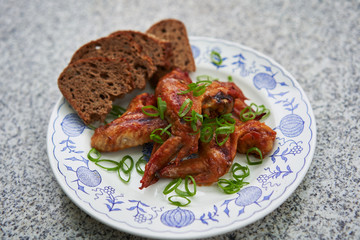 Spicy barbecue chicken buffalo wings marinated in soya sauce, ketchup, chili and honey served on the vintage rustic plate on stone table with green chopped fresh spring onion and whole grain bread.