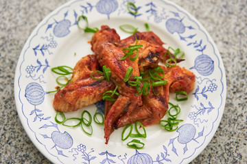 Close up Picture on the spicy barbecue chicken buffalo wings marinated in soya sauce, ketchup, chili and honey served on the vintage rustic plate on stone table with green chopped fresh spring onion.