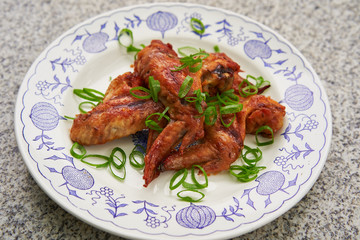 Close up Picture on the spicy barbecue chicken buffalo wings marinated in soya sauce, ketchup, chili and honey served on the vintage rustic plate on stone table with green chopped fresh spring onion.