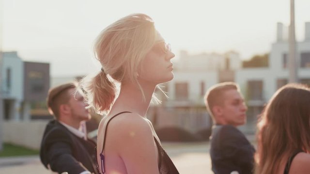 Profile of attractive blonde girl sitting among audience on seats outdoors. Close-up pretty business lady making bids for property raising hand showing paddle. Modern auction.
