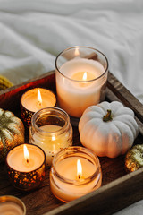 Burning candles pumpkin decoration on wooden tray with warm plaid in bed. Autumn style. Hygge...