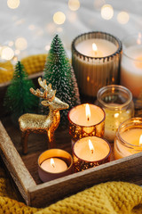 Burning candles and christmas decorations on wooden tray with warm plaid. Winter cozy style. Hygge concept.