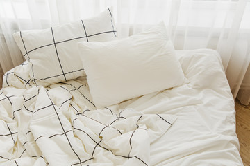White bedding sheets with striped blanket and pillow. Messy bed.