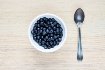 white ceramic bowl with blueberries, silver spoon on light wooden table