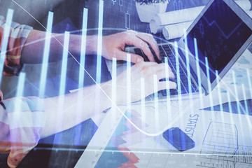 Double exposure of stock graph with businessman typing on computer in office on background. Concept of hard work.