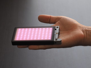 Portable RGB light on a man hand, dark background. Pink light.