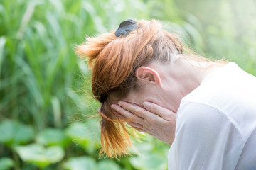 A depressed woman holds her hands in front of her face. She is sitting in a garden. Concept...