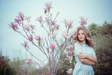 Obraz na płótnie Canvas Beautiful happy young woman enjoying smell in a flowering spring garden.Beutiful tree magnolias,big flowers. Blonde with blue eyes and blue dress.