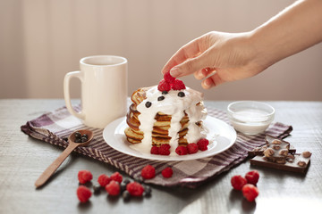 Fototapeta na wymiar Side view of delicious pancakes with fresh berries and sour cream, baker putting raspberrry on top of muffins stack, tasty breakfast for whole family, dessert for morning meal. Food concept.