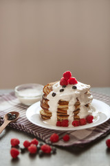 Side view of tasty pancakes in stack with sour cream and resh berries on white plate, muffins decorated with raspberries and blueberries, delicious pancacke for breakfast. Healthy eating concept,