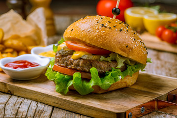 Burger with meat cheese and vegetables on the board on wooden table