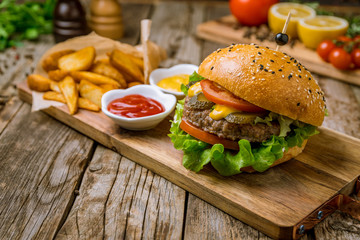 Burger with meat cheese and vegetables on the board on wooden table