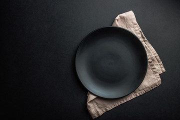 Elegant black table setting: plates, napkin and silverware over black background. Flat lay. copy...
