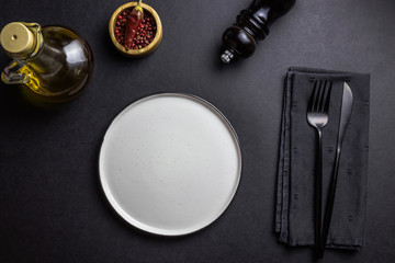 Elegant black table setting: plates, napkin and silverware over black background. Flat lay. copy space