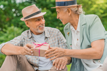 Positive senior woman looking at her husband while taking her present from him