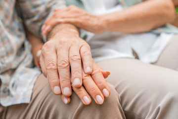 Loving senior couple sitting together and holding hands in a park. Close up image with focus on hands